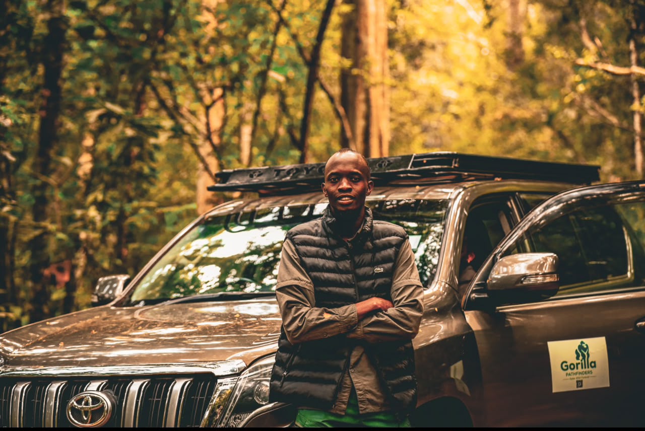 Safari guide standing with folded arms in front of a grey Gorilla Pathfinders vehicle in a forest