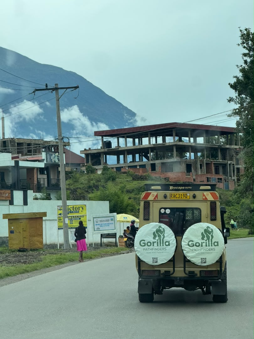 Gorilla Pathfinders safari vehicle driving toward mist-covered mountains on a rural road