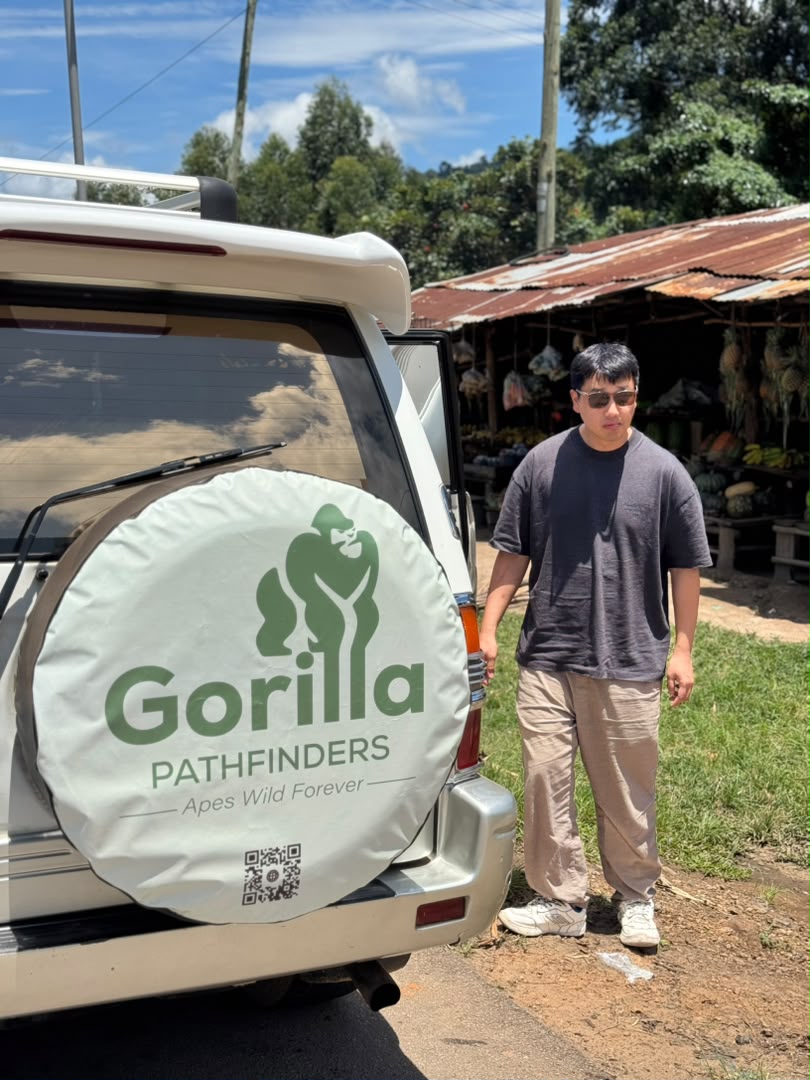 Male traveller beside a Gorilla Pathfinders safari vehicle near roadside market stalls