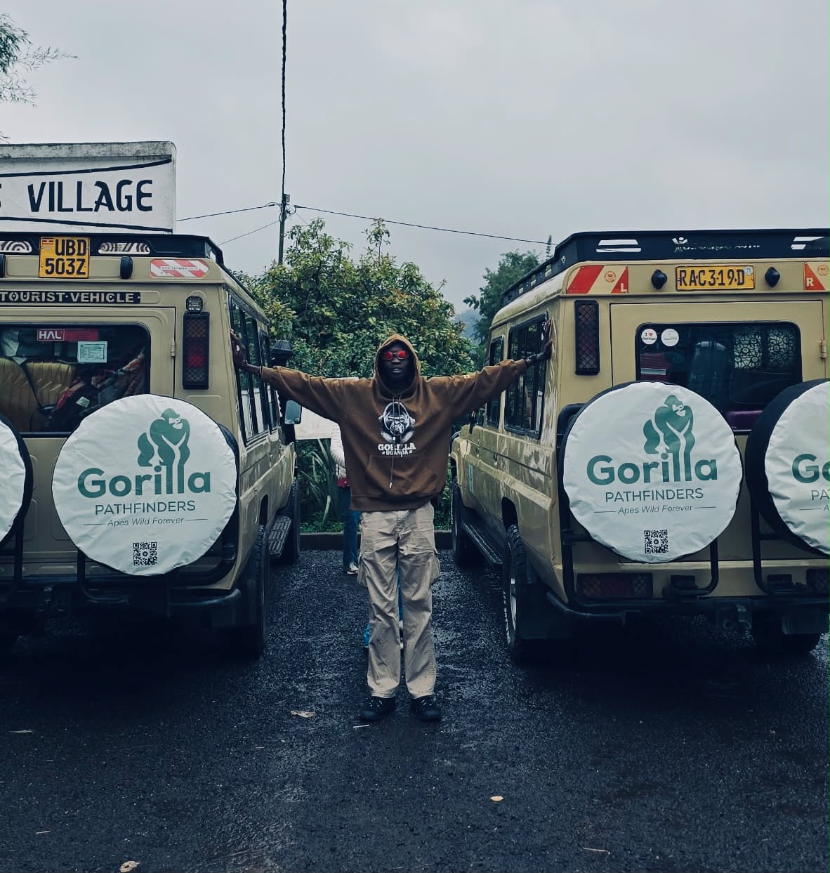 Gorilla Pathfinders team member standing between two beige safari vehicles on wet pavement