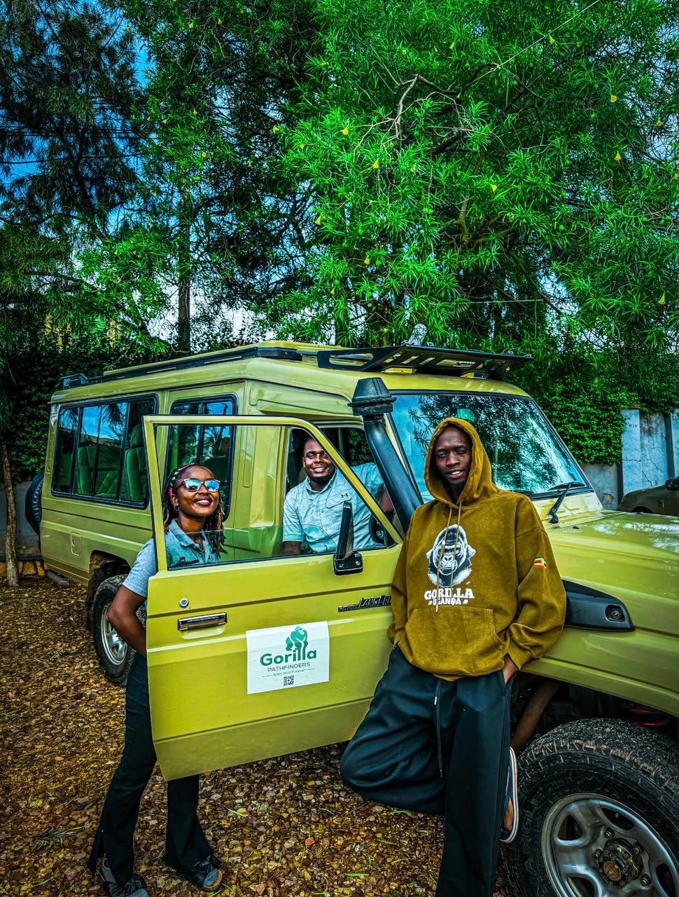 Three Gorilla Pathfinders team members posing with a beige safari Land Cruiser under trees