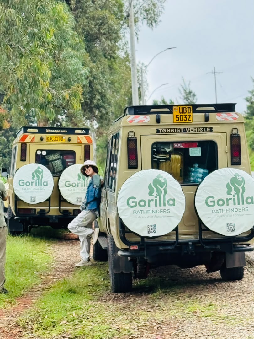 Woman posing beside two beige Gorilla Pathfinders vehicles on a lush forest track