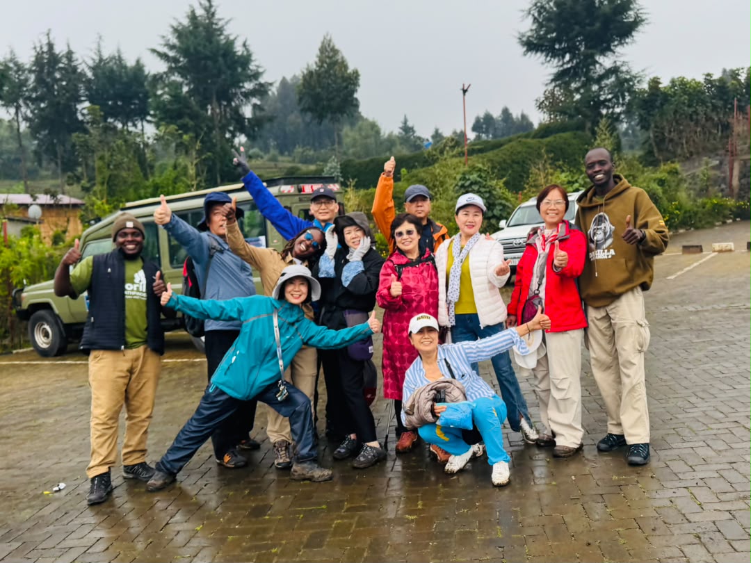 Large group of safari guests and Gorilla Pathfinders guides posing together with thumbs up
